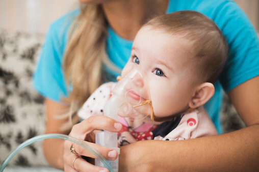 A concerned mother helps her baby use an inhaler with a mask, providing relief from respiratory symptoms.