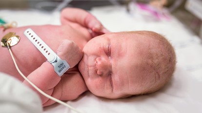 A tiny, swaddled newborn baby sleeps peacefully in a hospital crib