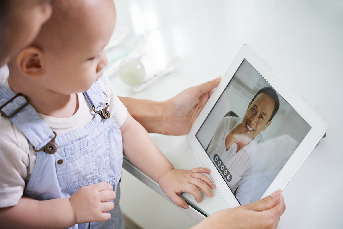 A mother, holding her baby, participates in a virtual telemedicine appointment with a pediatrician, utilizing technology to ensure timely and convenient healthcare for her child.