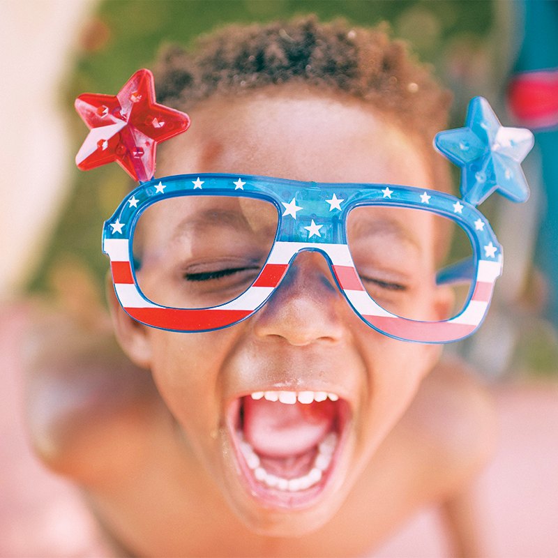 A stylish young boy, sporting oversized patriotic sunglasses, enjoys a sunny day, looking cool and confident.