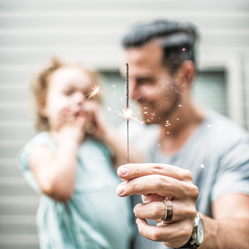 A father and child, standing close together, light up sparklers, celebrating a special occasion with a sense of wonder and excitement.