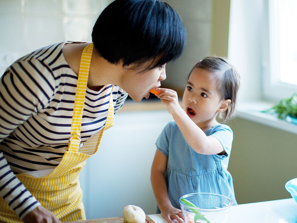 A sweet child, eager to share, offers a carrot to her parent.