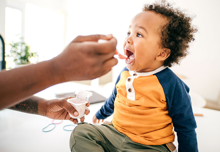 A caring father gently feeds his baby yogurt.