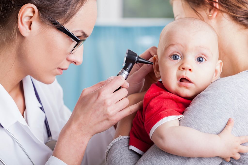 A pediatrician carefully examines a child's ear canal with an otoscope.