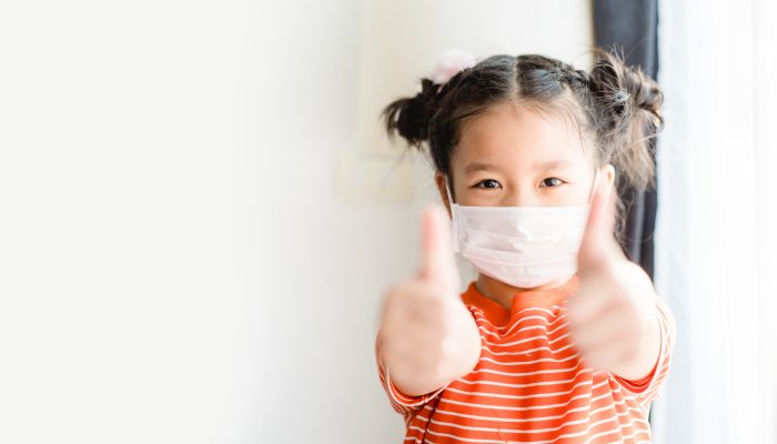 Little girl wearing mask holding two thumbs up