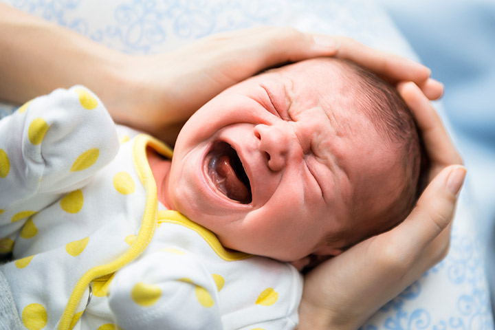 A concerned mother gently cradles her colicky baby's head, offering comfort and support during a painful episode.