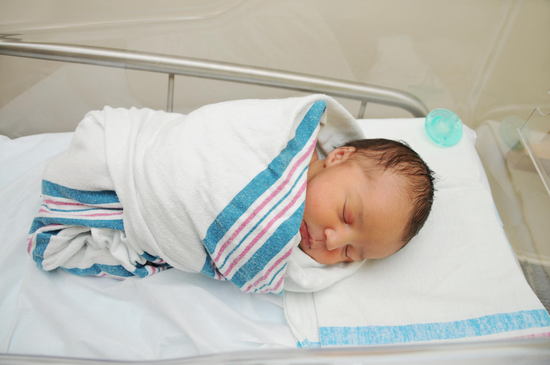 A tiny, swaddled newborn baby rests peacefully in a hospital crib.