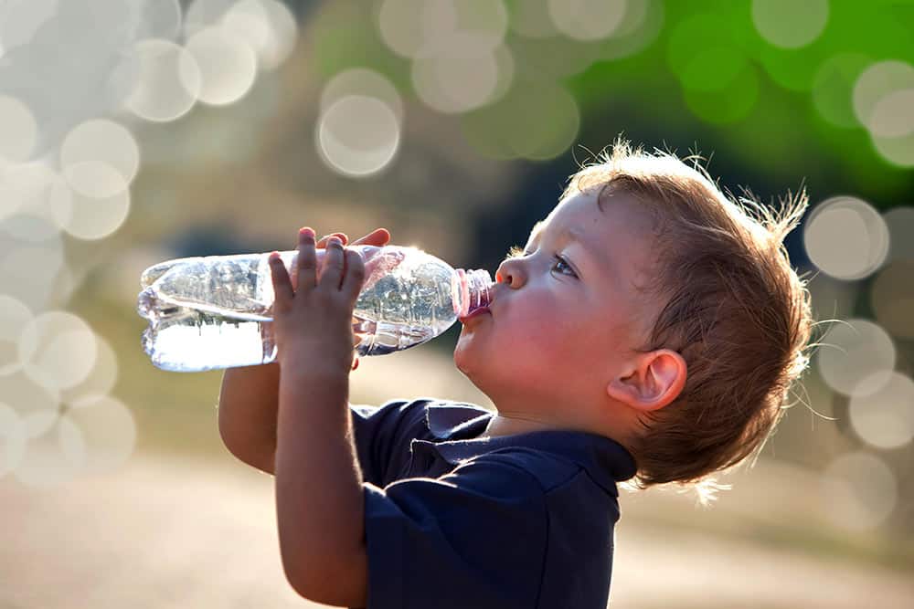 A thirsty child quenches their thirst by drinking water from a reusable water bottle.