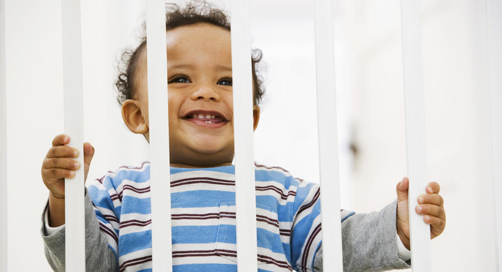 A happy, curious child stands confidently on their crib, exploring their surroundings and taking a step towards independence.