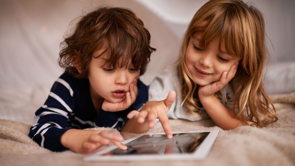 Two children, engrossed in a shared digital experience, sit side-by-side, navigating a tablet.