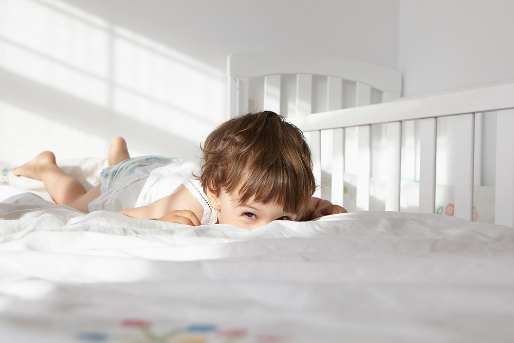 A joyful child playfully rolls on the bed, enjoying a moment of carefree fun.