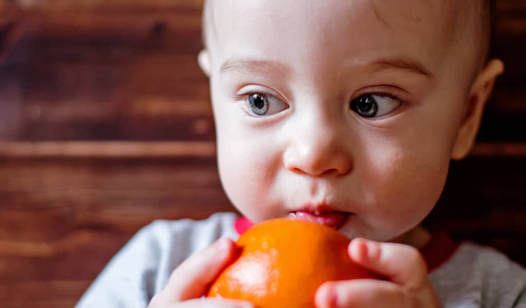 A child, with a rash developing on their face, eats an orange, highlighting a potential food allergy reaction.