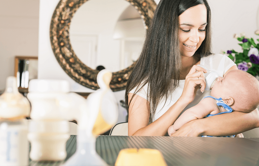 A loving mother smiles as she gently feeds her baby with a bottle of milk.