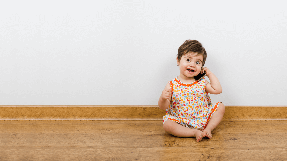 Happy baby sitting on the floor and talking on the phone