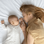 A parent falling asleep while trying to help her baby that is fighting sleep