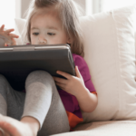 A young toddler sits and interacts with content on an iPad screen.