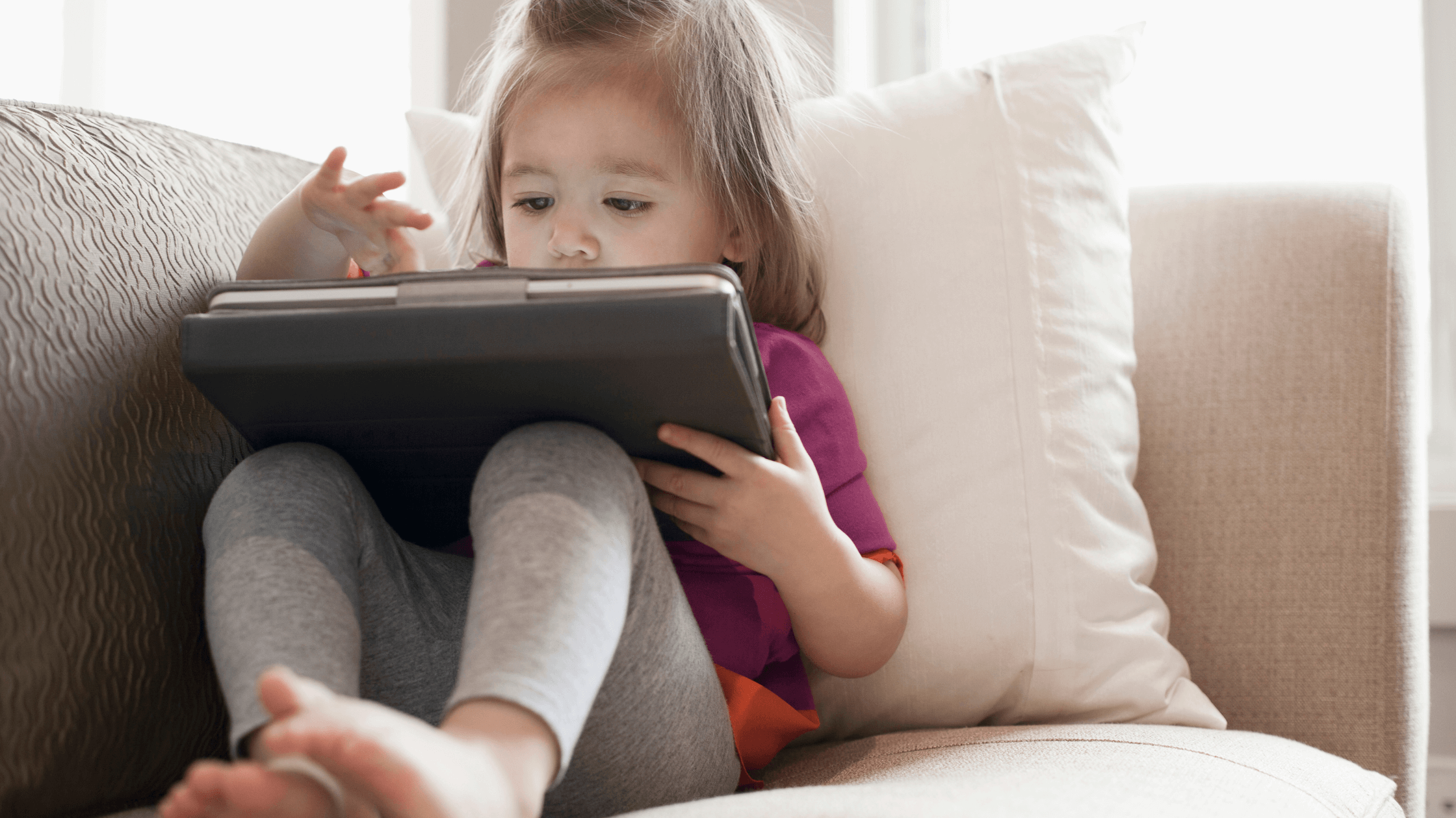 A young toddler sits and interacts with content on an iPad screen.