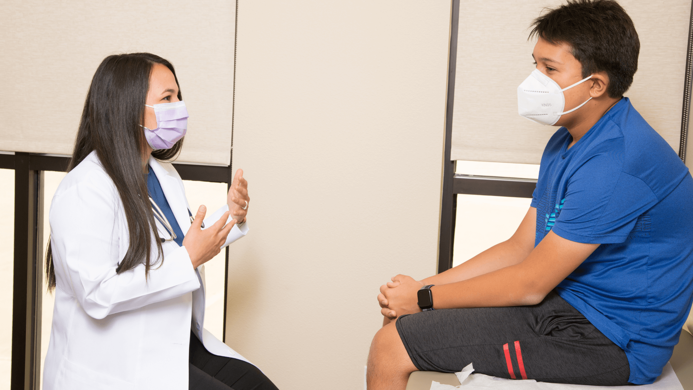 A pediatrician wearing a mask consults with a young boy wearing a mask during a well-child visit.