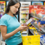A woman in a supermarket aisle reads a food label on a product, focusing on child nutrition.