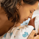 A new mother gently cradles and looks at her newborn baby's face, nose to nose, in a hospital setting.