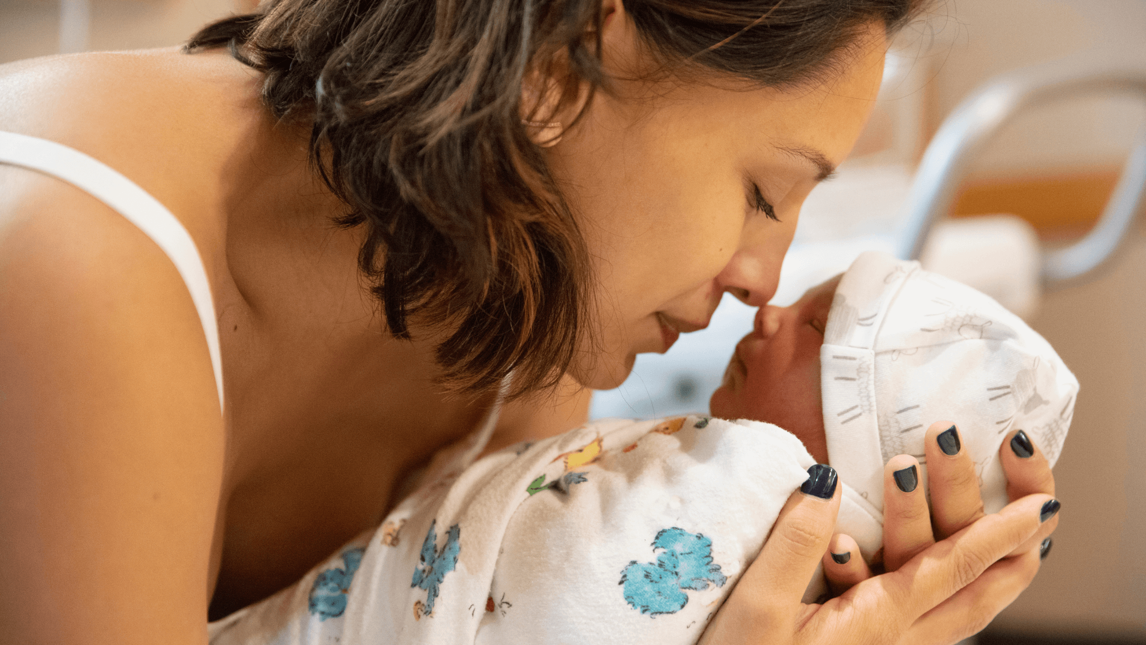 A new mother gently cradles and looks at her newborn baby's face, nose to nose, in a hospital setting.